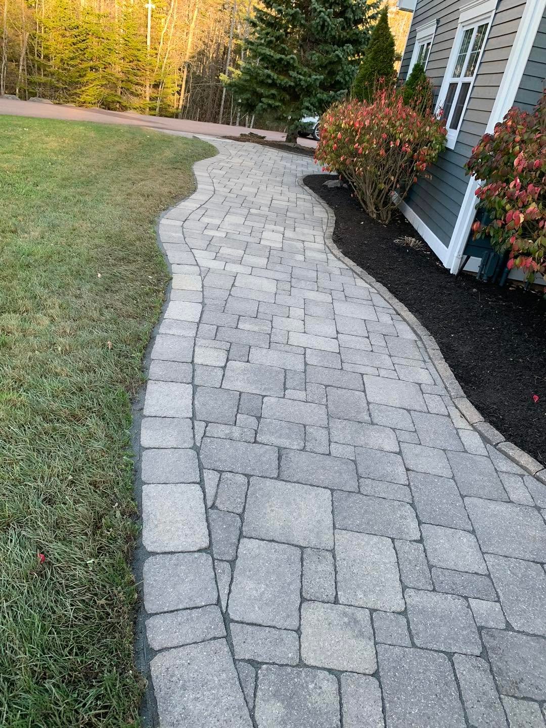 Curved grey paver walkway through a landscaped yard